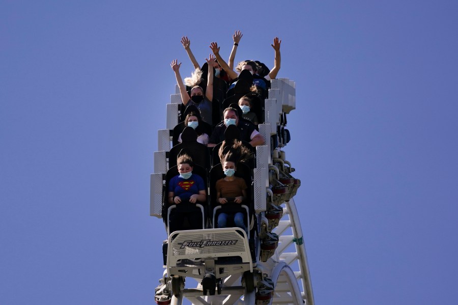 FILE - Visitors wearing masks ride on a roller coaster at Six Flags Magic Mountain on its first day of reopening to members and pass holders in Valencia, Calif., on April 1, 2021. Cedar Fair and Six Flags Entertainment Corp. are merging, creating an expansive amusement park operator with operations spread across 17 states and three countries. (AP Photo/Jae C. Hong, File)